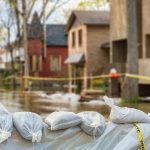 Close Shot Of Flood Protection Sandbags With Flooded Homes In The Background